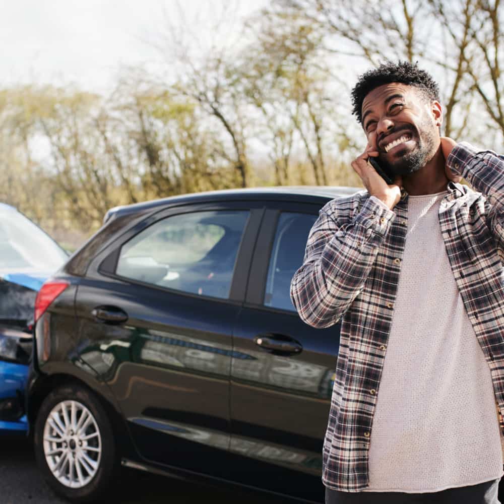 Young man standing next to a wrecked car.