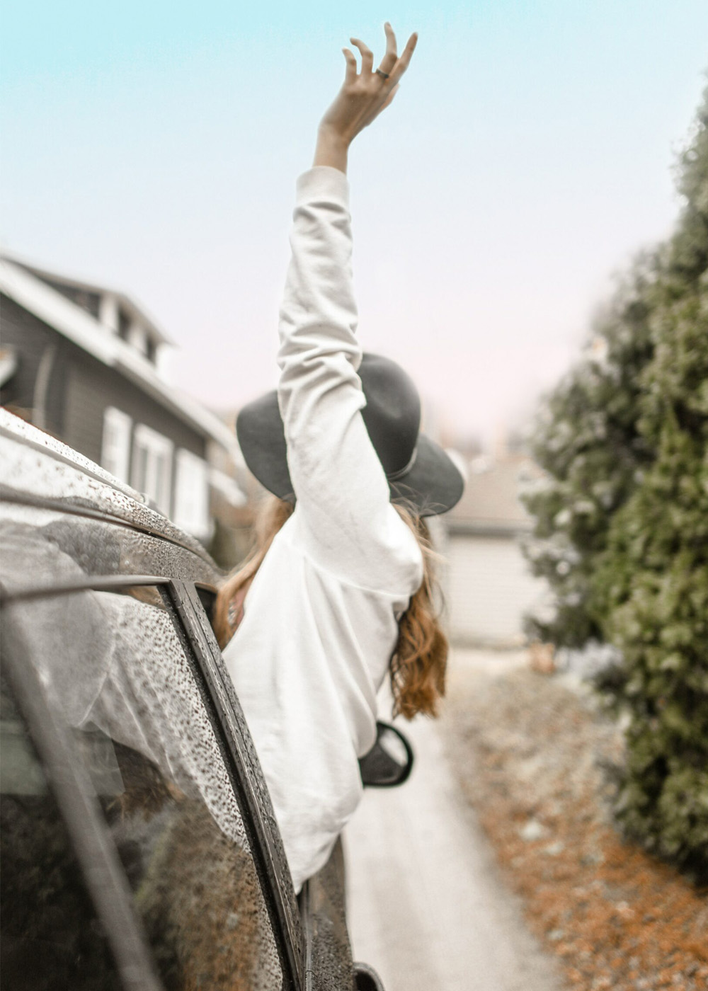 Youg girl riding in car hanging out window waving.