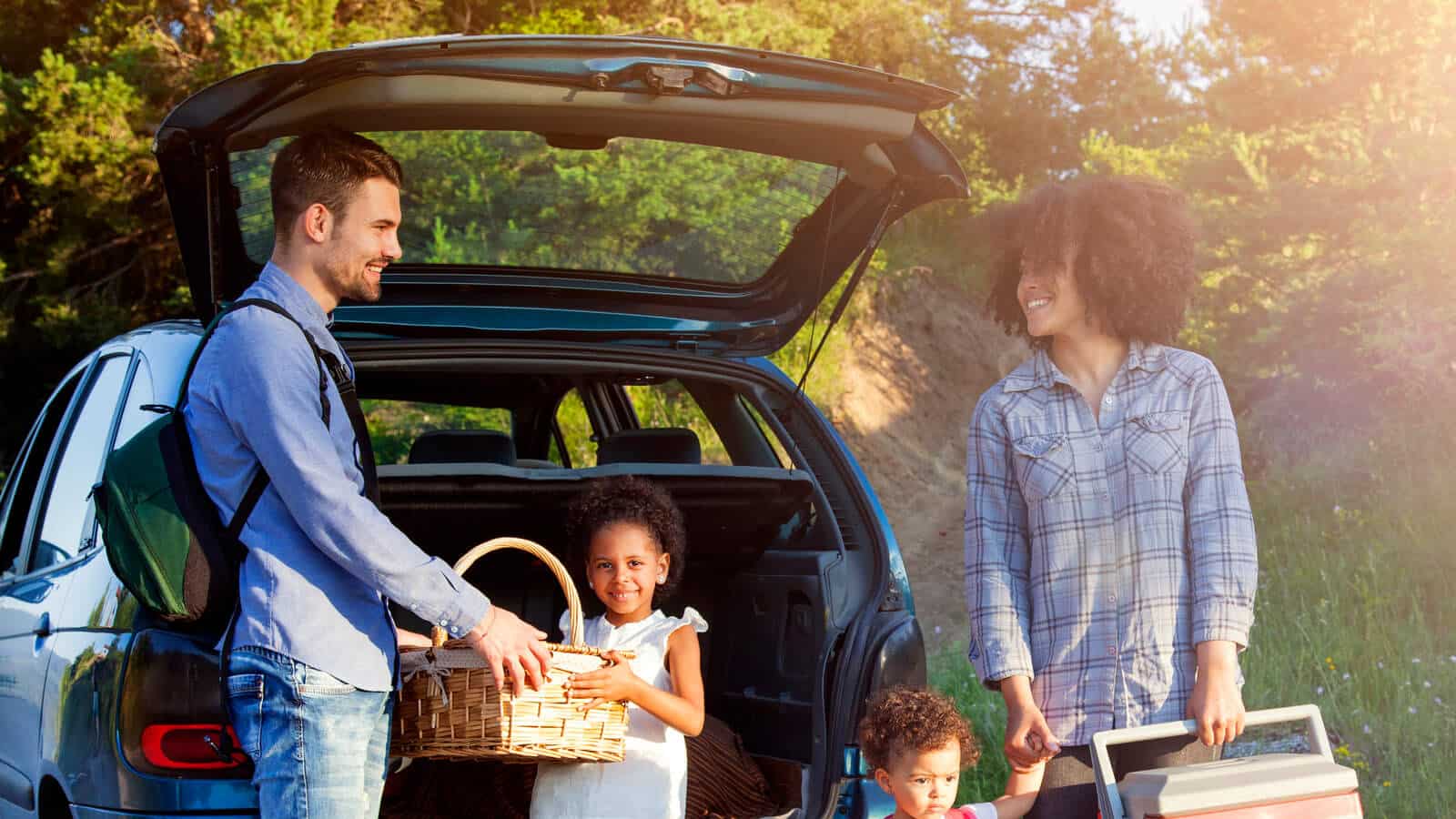 A family going on a picnic. They are standing near a new car.