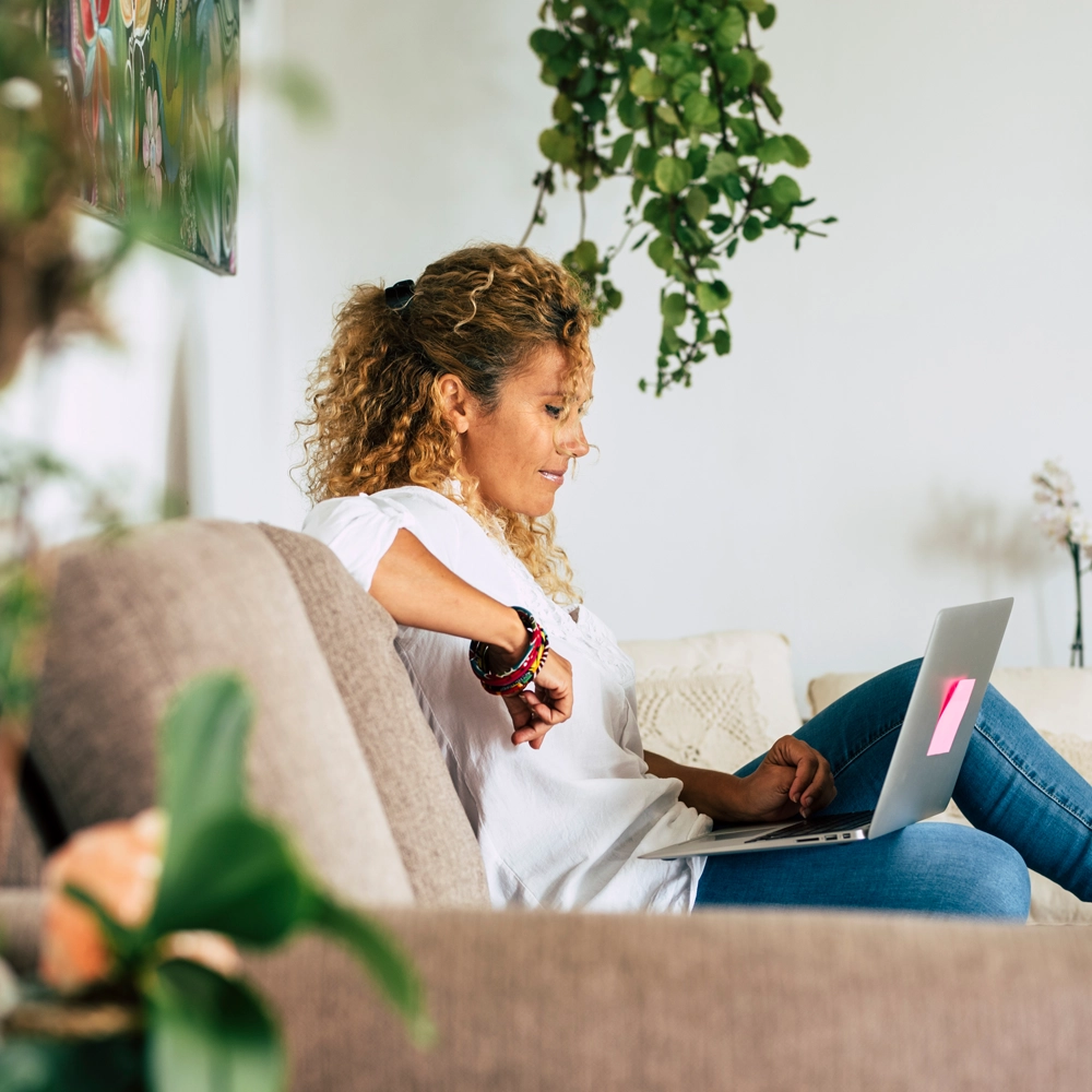 Lady sitting on her couch look at a laptop.