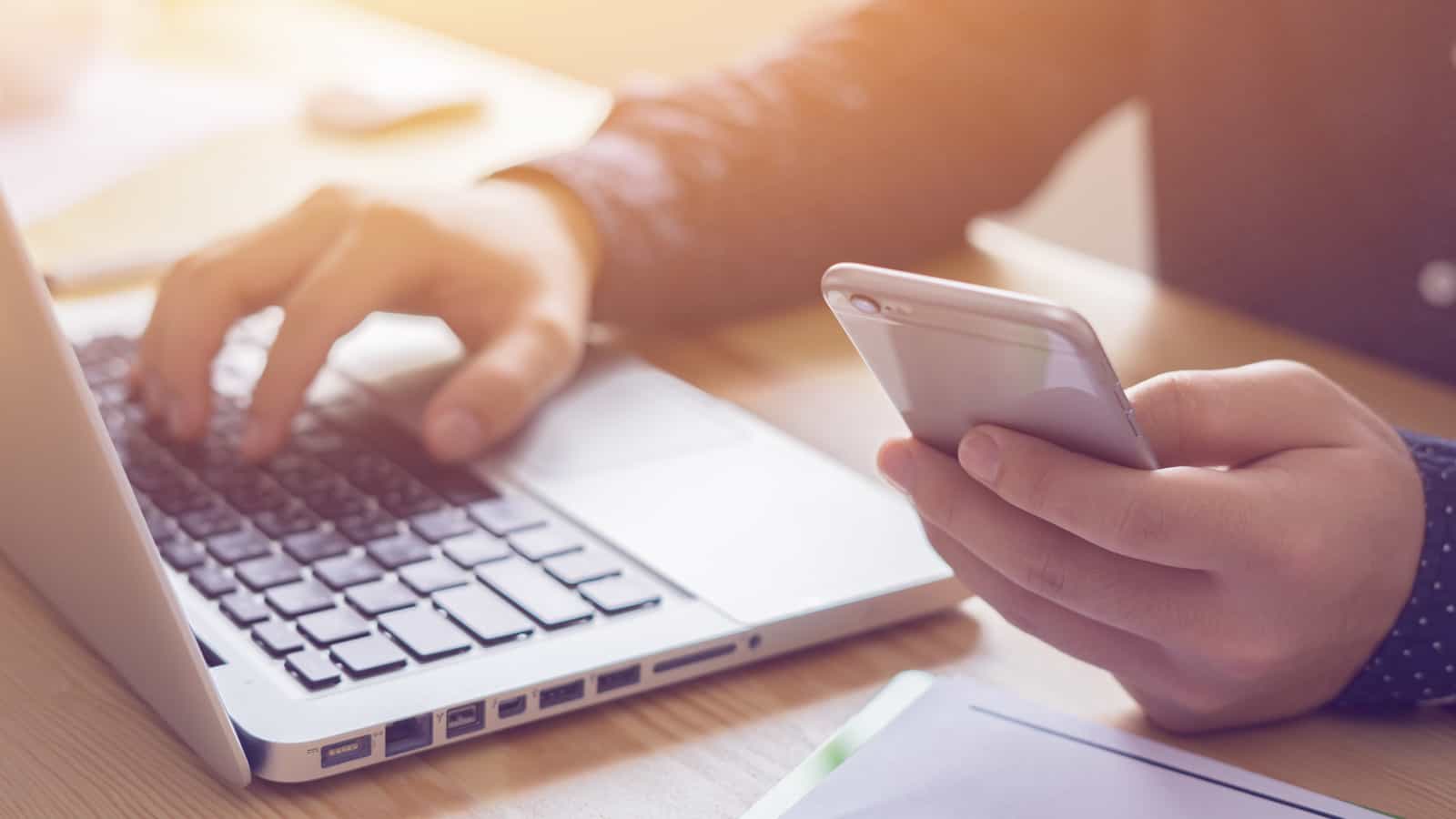 Photo of hands on a phone. Laptop next to the person