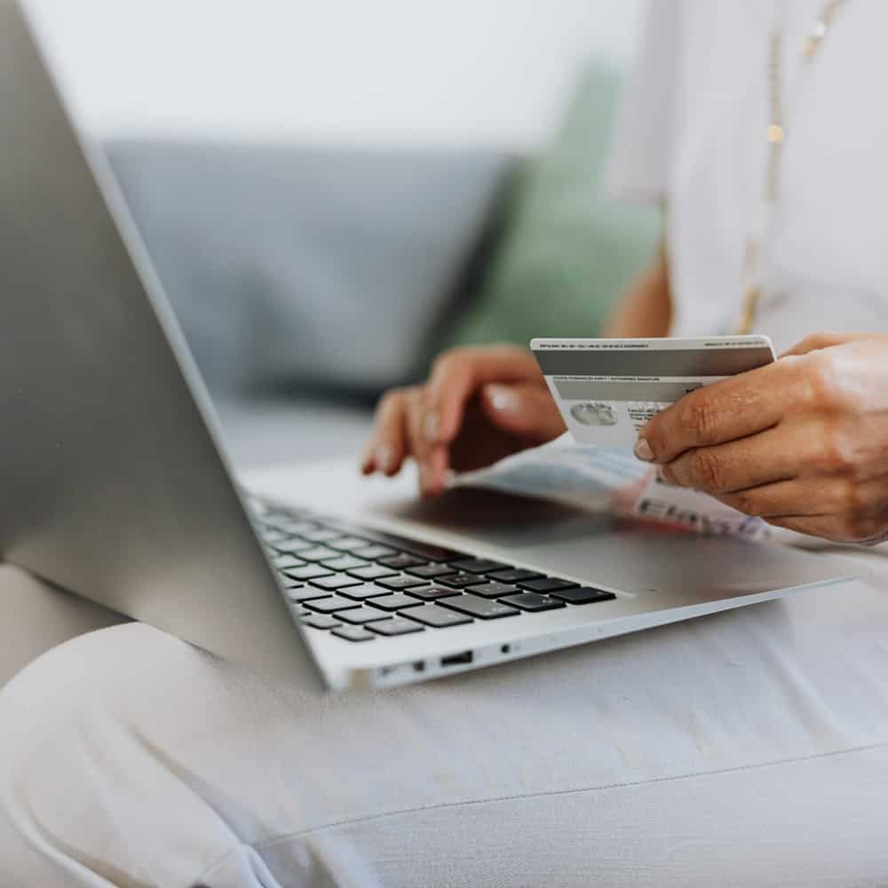Older woman using laptop while looking at credit cards.