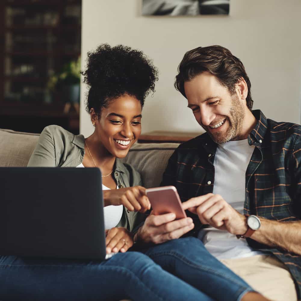 A couple sitting on a couch looking at a laptop.
