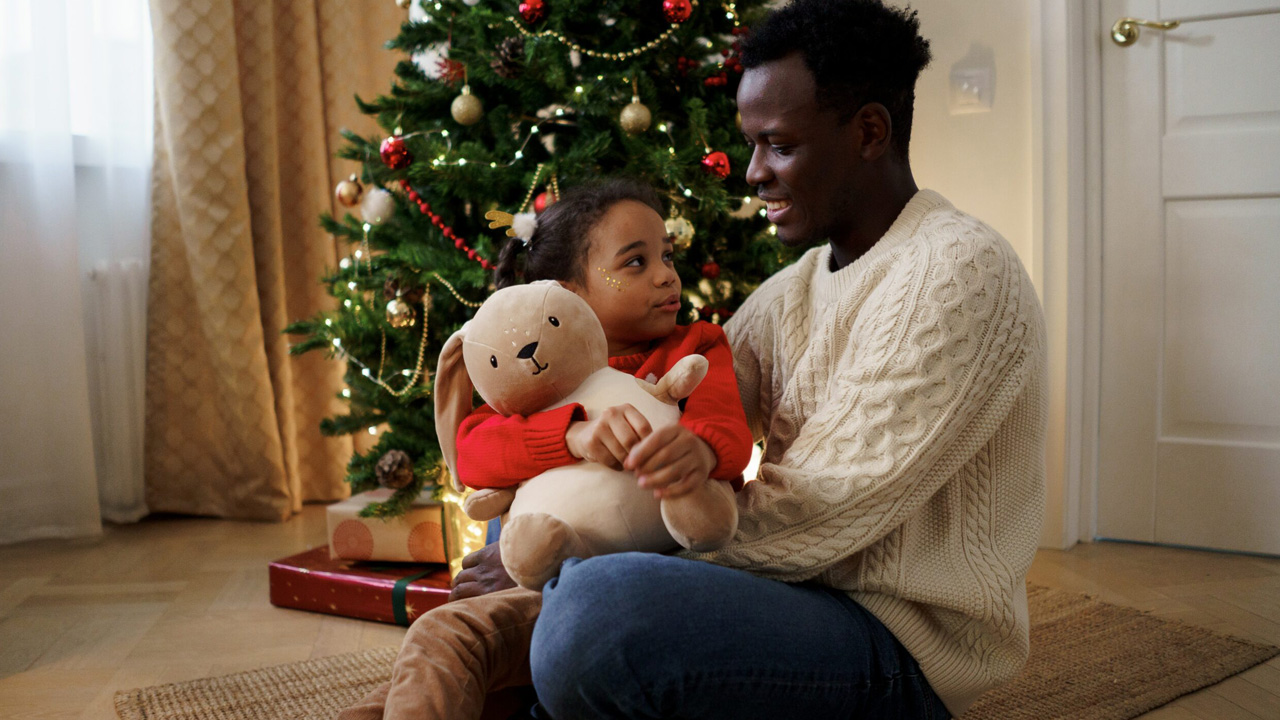 Father sitting next to Christmas tree with his daughter.